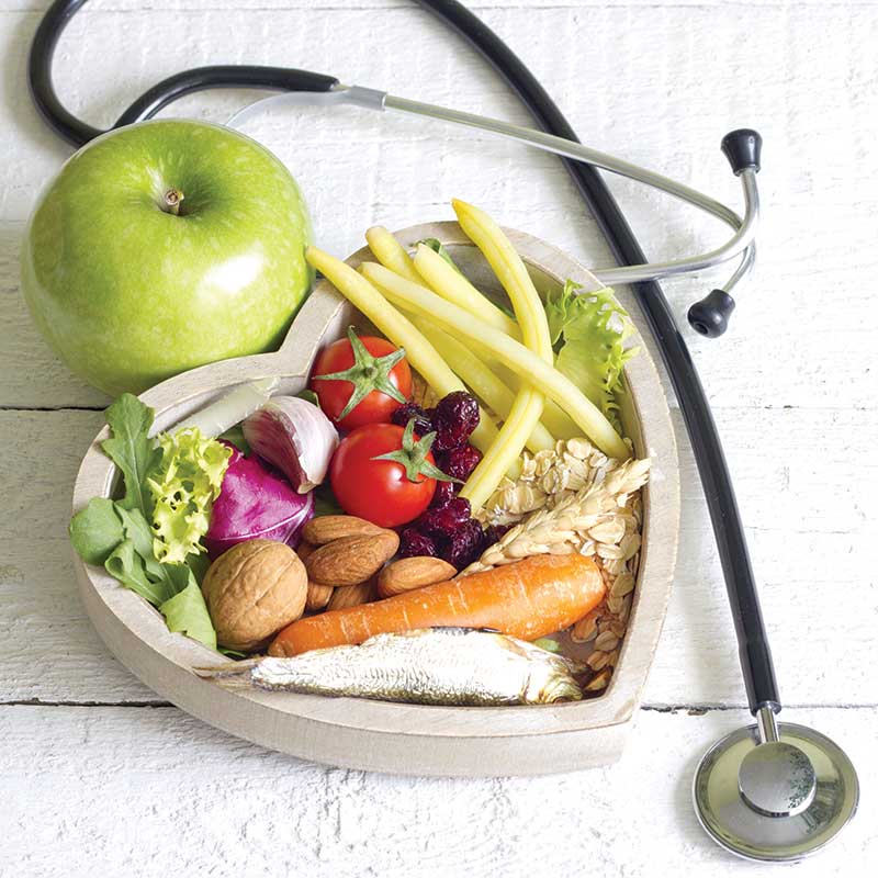 Nutritious fresh foods and seafood in a heart-shaped wood container surrounded by a stethiscope.