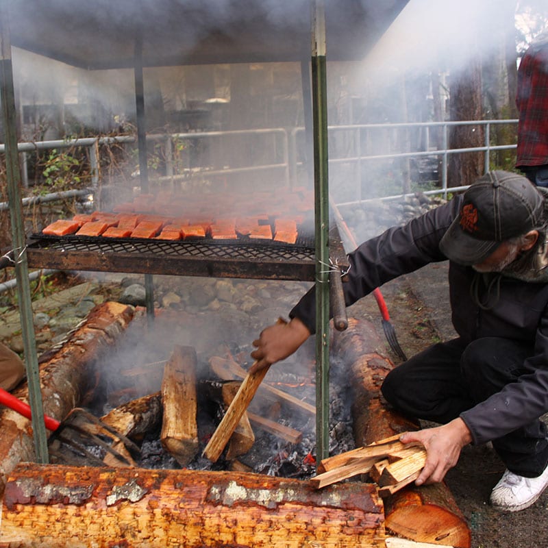 Members of the Muckleshoot Tribe cook wild salmon in a traditional preparation over a fire pit at a 2017 community gathering to learn about the effects of GE salmon. Photo credit: Johanna Lundahl photography.