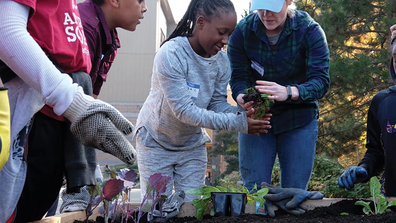 Young girls and boys gardening with a teacher